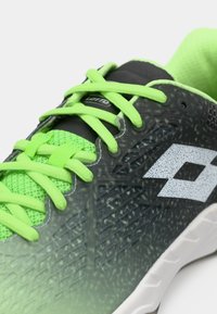 Detailný záber na zelenú a čiernu športovú obuv s jasne zelenými šnúrkami a bielym geometrickým logom na boku.