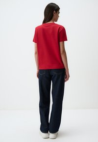 T-shirt di cotone rossa con maniche corte, vestibilità comoda, abbinata a jeans a vita alta di colore blu scuro e sneakers bianche. Design semplice, senza fantasie.