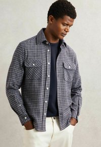 Cămașă din flanel în carouri pentru bărbați, în nuanțe de bleumarin și gri, cu două buzunare la piept, închidere cu nasturi și guler. Textură netedă.