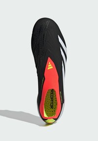 Chaussure de football noire avec un col en tricot rouge ajusté, des accents blancs, une surface texturée et un intérieur rembourré jaune avec un motif à pois.