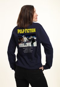 Donkerblauwe sweatshirt met lange mouwen, voorzien van een grafische print van een dansscène uit "Pulp Fiction" met gele tekst erboven en zwarte tekst eronder.