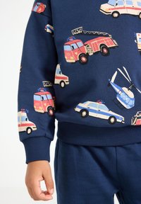 La felpa blu navy presenta stampe colorate di veicoli di emergenza, inclusi camion dei pompieri ed elicotteri, con polsini e orlo a coste.