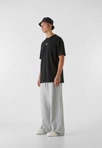 Black cotton t-shirt with a crew neck and white text. Gray wide-leg sweatpants, white slip-on shoes, and a black bucket hat.