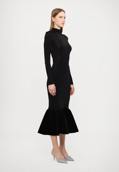 Sort langærmet kjole med et tætsiddende bodice og en flared fløjlssøm. Sammen med sølvfarvede spidse hæle. Glat tekstur hele vejen igennem.