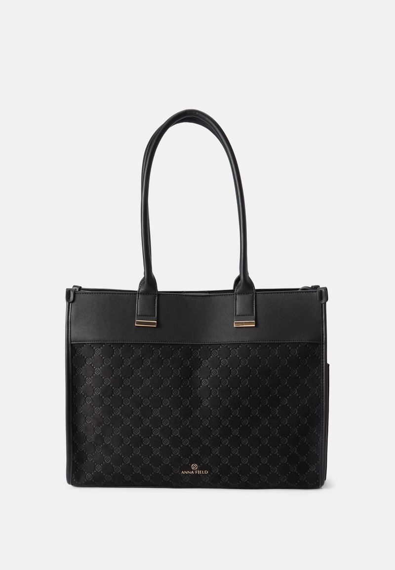 Black tote bag with a textured patterned lower half, smooth upper half, dual handles, and gold-tone hardware accents. Features logo on front.