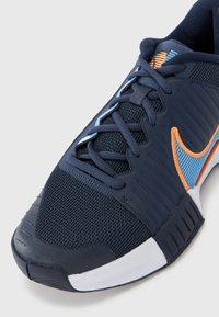 Marineblaue Sportschuh mit Mesh-Obermaterial, orangefarbenen und blauen Akzenten, flachen Schnürsenkeln, strukturiertem Gummisohle und verstärkter Zehenkappe.
