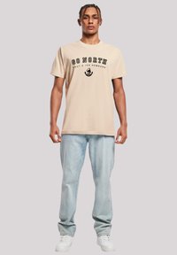 Beige cotton t-shirt with "GO NORTH" text and central graphic, paired with light blue jeans and white sneakers.