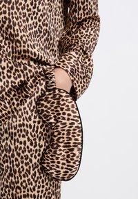 Blusa de estampado de leopardo en tejido sedoso con mangas largas y detalle fruncido en el puño. El bolsillo presenta un diseño redondeado con ribete negro.