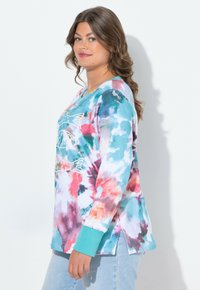 Farbiger Batik Langarmshirt mit türkisfarbenen Bündchen und V-Ausschnitt, mit Fischgrafik auf der Vorderseite und seitlichen Schlitzen am Saum.