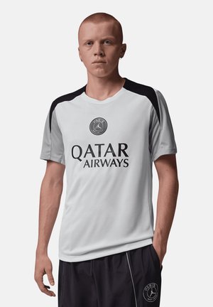 Uomo con capelli rossi corti che indossa una maglia sportiva bianca e nera del Paris Saint-Germain con il logo Qatar Airways e pantaloncini neri.