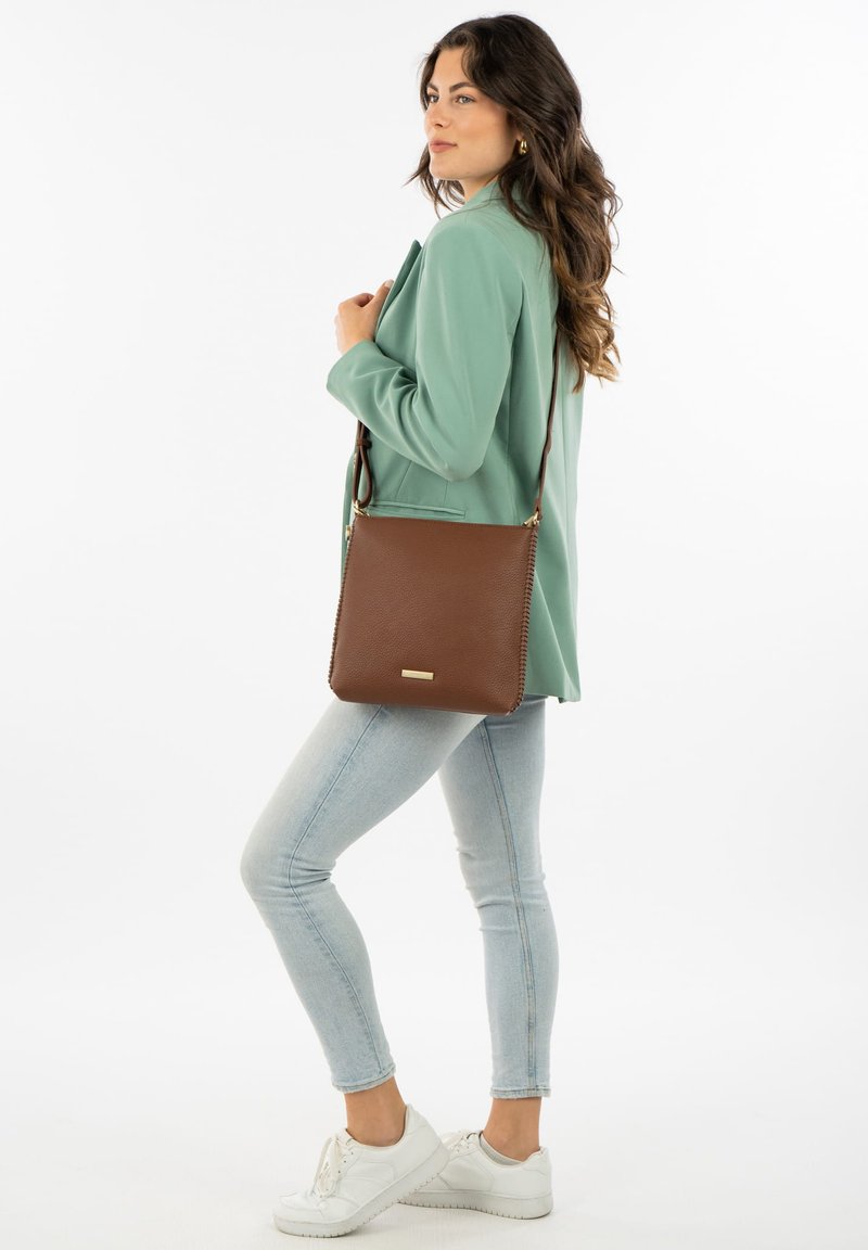 Bruine leren crossbodytas met een gestructureerde afwerking, gouden hardware accenten, rechthoekige vorm en gestikte details. Draagt een mintkleurige blazer.