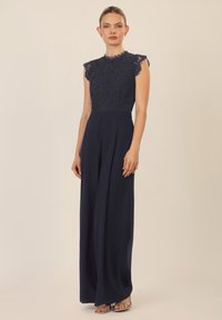 Mono marinero con un corpiño de encaje y mangas cortas, pantalones plisados y fluidos, y una cintura ajustada. Tejido suave con una intrincada textura de encaje.