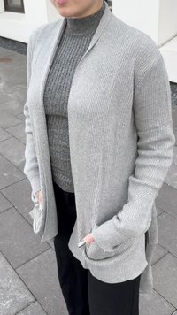 Világosszürke, bordázott kardigán nyitott elülső résszel, hosszú ujjak és zsebek. Egy szürke, texturált garbó fölé rétegezve. Simogató, puha szövettextúra.