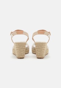 Wedge sandals with a woven rope heel. White patent upper with a tan ankle strap and buckle. Textured back and solid, stacked heel design.