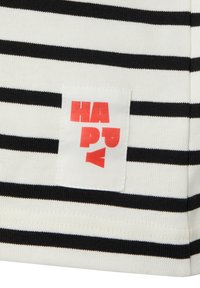 Schwarz-weiß gestreifter Baumwollstoff mit einem quadratischen weißen Etikett, auf dem „HAPPY" in fettem rotem Text steht. Der Stoff ist strukturiert und sitzt eng an.