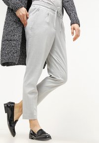 Ljusgrå, avsmalnande byxor med elastisk midja och dragsko. Bärs med en strukturerad svart cardigan och svarta loafers. Slät tyg.