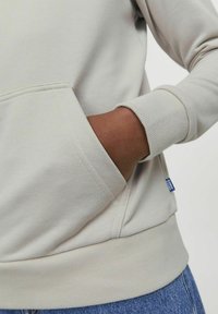 Felpa grigia chiara con polsini e orlo a coste, dotata di una tasca frontale. Tessuto liscio con minimal branding nell'angolo in basso.