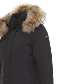 Cappotto invernale nero con colletto in pelliccia sintetica, dotato di chiusura con zip e bottoni, tasche laterali e una toppa con logo sulla manica.