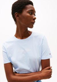 Svijetloplava pamučna majica s okruglim izrezom i kratkim rukavima, s printanim "Tommy Hilfiger" logotipom u bijeloj boji na prednjoj strani.