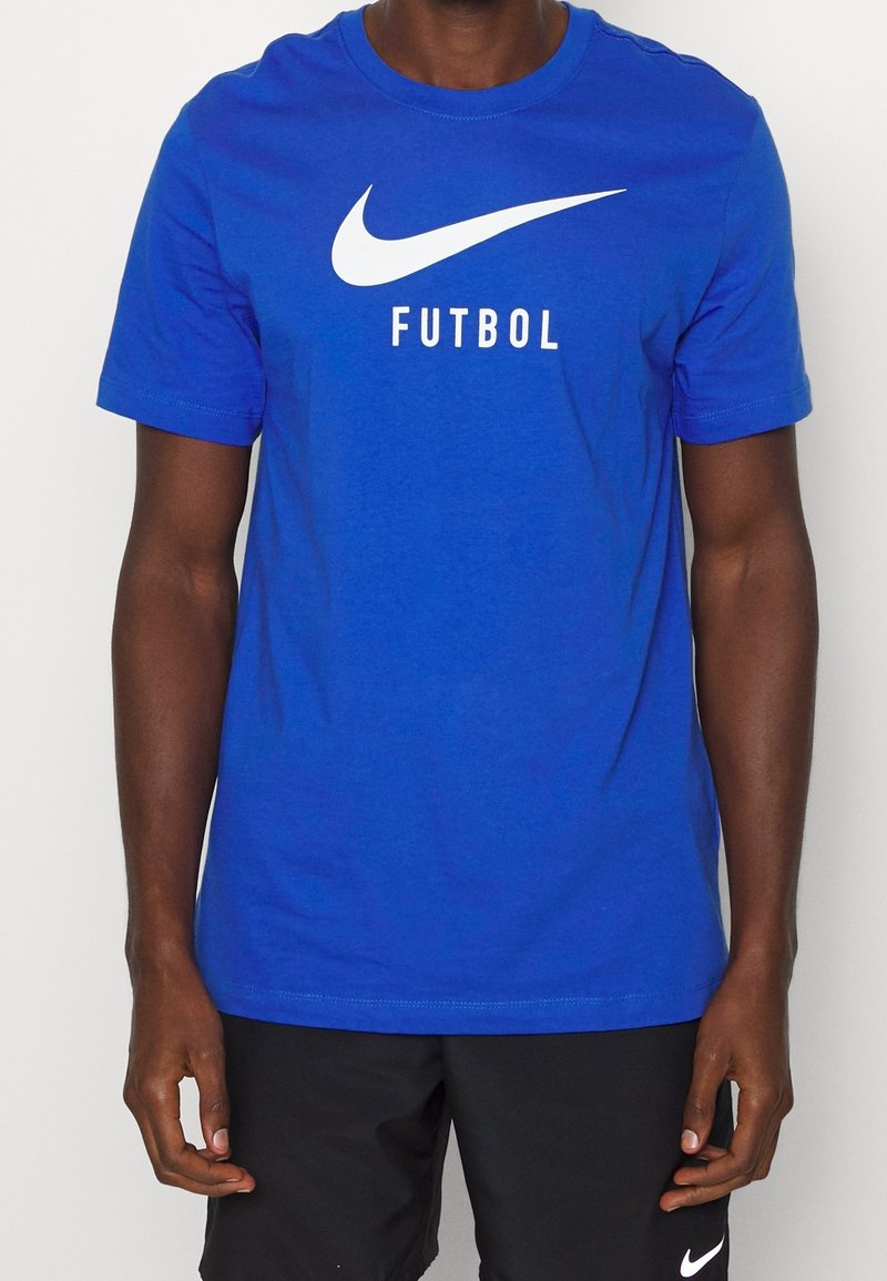 Modré bavlněné tričko s velkým bílým logem Nike a slovem "FUTBOL" tučnými černými písmeny, s krátkým rukávem a kulatým výstřihem.