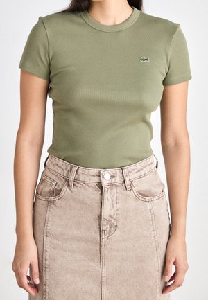 Olivgrünes, geripptes Kurzarm-T-Shirt mit Rundhalsausschnitt, kombiniert mit einem hellbeigen Jeansrock. Mit kleinem, gesticktem Logo.