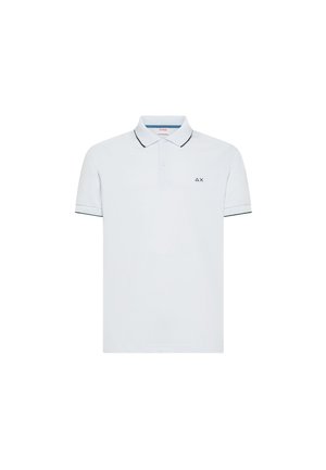 Polo blanco de manga corta con ribetes negros en el cuello y los bordes de las mangas, botones en el cuello y un pequeño logo negro en forma de triángulo y X en el pecho.