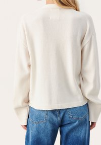 Crème-kleurige, gebreide trui met een relaxte pasvorm, geribbelde manchetten en zoom. Gecombineerd met lichtblauwe, high-waisted denim jeans.
