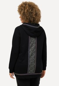Sudadera negra hecha de un tejido suave, con un panel de patrón geométrico en la parte posterior y acentos contrastantes a lo largo de los bordes.