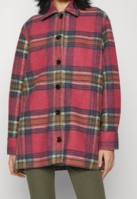 Plaid wool shirt jacket in pink and green hues, featuring a collar, long sleeves, and dark buttons along the front closure.