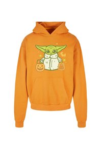 Oranžová mikina s kapucí a kapsou, která zobrazuje grafiku postavy držící Halloweenové dýně a hvězdy.