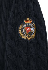 Marinblå stickad tröja med en strukturerad kabeldesign och en broderad polo klubb-logotyp med guldaccenter på vänster ärm.