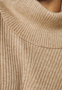 Gerippter Rollkragenpullover in hellem Beige mit strukturierter Oberfläche. Verfügt über einen gemütlichen, breiten Kragen und einen dezenten Glanz im gesamten Stoff.