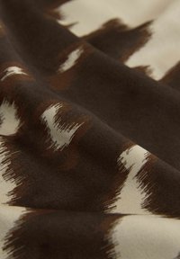 Tissu avec une texture lisse et douce présentant un mélange de motifs abstraits de coups de pinceau marron et crème. Pas de coutures ni de matériel visible.