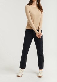 Beige long-sleeve sweater in soft fabric paired with high-waisted black jeans and white sneakers. Simple design with ribbed cuffs and hem.