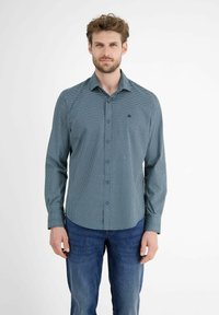 Langsleeve overhemd met knopen in teal met een klein wit stippenpatroon, gecombineerd met blauwe jeans. Heeft een puntige kraag en een borstzak.