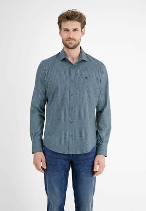 Langsleeve overhemd met knopen in teal met een klein wit stippenpatroon, gecombineerd met blauwe jeans. Heeft een puntige kraag en een borstzak.