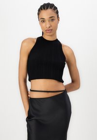 Top corto de halter negro con diseño ajustado. Combinado con una falda de satén negro suave que presenta una sutil abertura lateral.