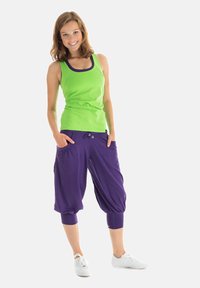 Green sleeveless top with purple trim, paired with loose purple harem pants featuring side pockets, worn with white athletic shoes.