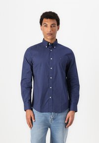 Marineblauw, langemouw shirt met witte stippen, met knoopsluiting, en witte knopen, gecombineerd met lichtblauwe denim jeans.