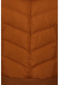 Brun quiltet stof med vandret og chevron-syninger samt en ribbet strikkant i bunden.