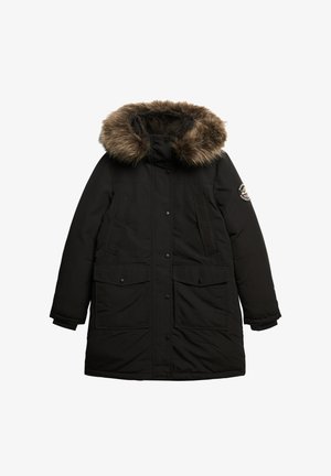 Parka noire avec une capuche doublée de fausse fourrure, fermeture éclair et pressions, deux poches avant et un écusson sur la manche.