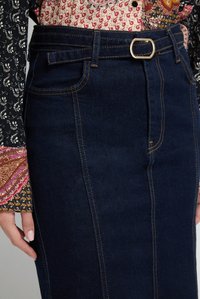 Falda de mezclilla azul oscura con detalles de costura visibles, pasadores para cinturón y una hebilla plateada. La tela tiene una textura suave.