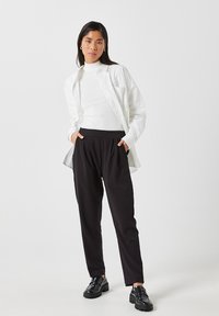 Balta krekls pār pieguļošu balto turtleneckreklu, kombinēts ar brīviem melniem biksēm un melniem loafers. Gludas tekstūras ar neitrālām krāsām.