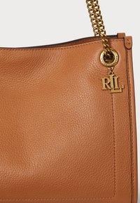 Χειροποίητη τσάντα σε καφέ δέρμα με υφή κοκκώδους. Διαθέτει χρυσό αλυσίδα και χρυσή διακόσμηση με τα γράμματα "RL". Μεγάλο ορθογώνιο σχήμα.