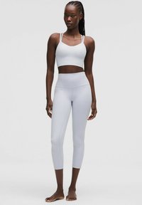 Un sutien sport de culoare gri deschis și leggings cu talie înaltă, ambele realizate dintr-un material elastic. Sutienul are bretele subțiri; țesătura este netedă.