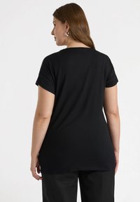 Schwarzes T-Shirt mit kurzen Ärmeln, lockerem Schnitt, rundem Ausschnitt und glatter Textur, das leicht über die Hüften reicht. Einfaches und unifarbenes Design.