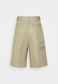 Shorts de travail beige arrivant aux genoux avec passants de ceinture, poches arrière à boutons, poche utilitaire sur le côté, et un petit écusson orange sur le côté droit.