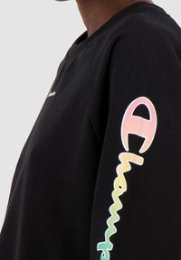 Felpa nera con collo a giro, maniche lunghe e un design colorato del logo sulla manica sinistra che riporta la parola "Champion".