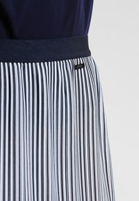 Pleated skirt with a navy waistband; features vertical black and white stripes; made of lightweight fabric with a smooth texture.