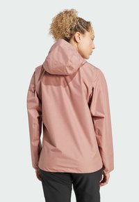 Giacca leggera rosa chiaro resistente all'acqua, con cappuccio, maniche lunghe e una texture liscia. Presenta una vestibilità comoda e un design minimalista.